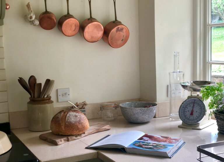 Image of country kitchen with copper pots, and wood counters. Plants and an egg timer are on the counter, as well as some recipe books. Photo by Cat Preston on Unsplash