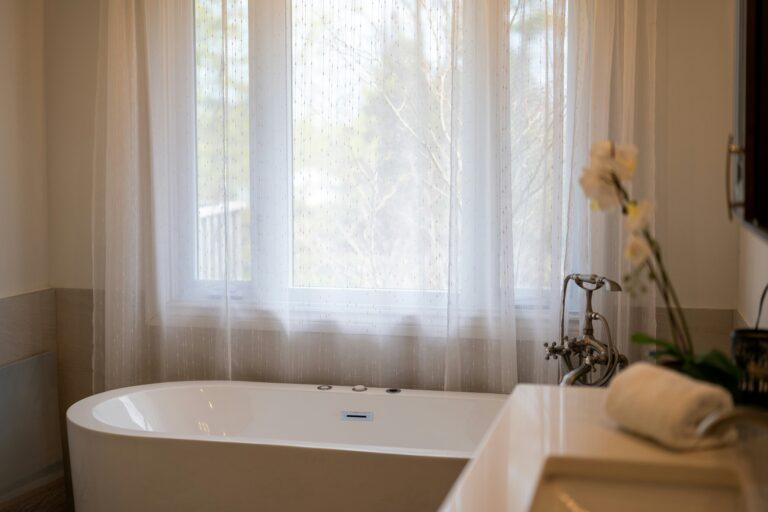 Processing grief and widowhood for Jess and Ryan Ronne. Image is of a beautiful tub with a curtained window, the tub is empty, and awaiting use. Photo by Franco Debartolo on Unsplash