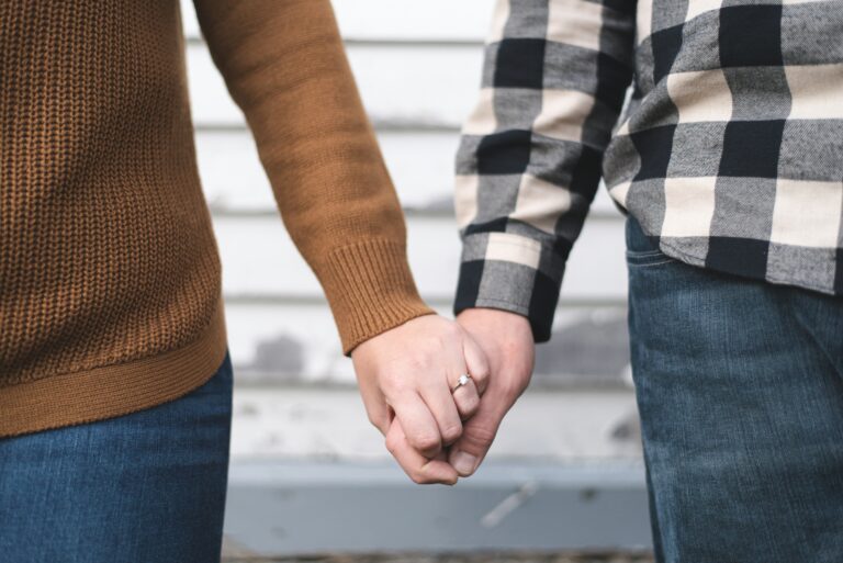 Couple holding hands. Woman is wearing a toffee long-sleeve sweater and jeans. Man is wearing a black and white plaid flannel and jeans.