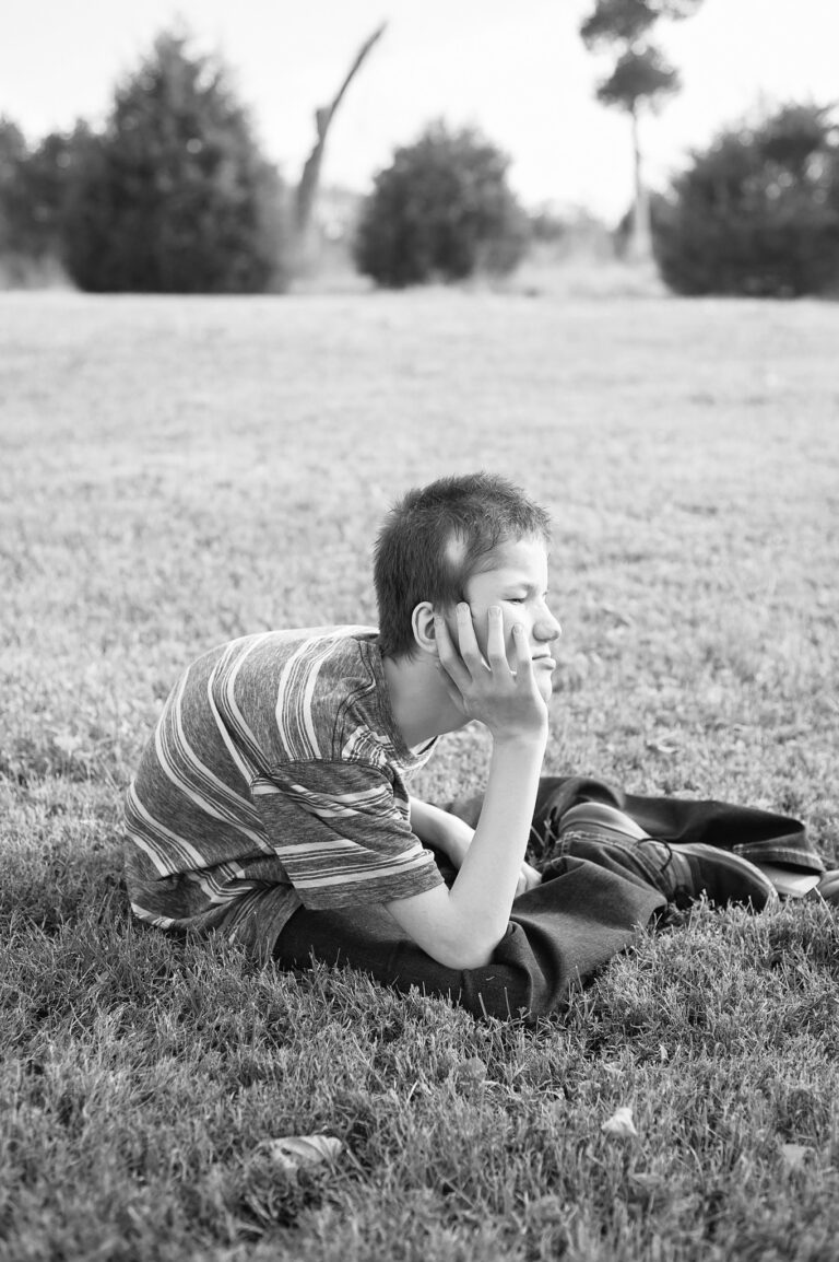 Lucas, beautiful broken boy, at Hope Farms sitting propped on his hand, in a field.
